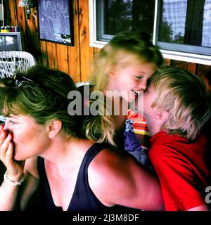 Mutter hält inne, während ihr achtjähriger Sohn seine zweijährige Schwester am Sebago Lake, Maine, küsst.; Sebago Lake, Maine, USA. Stockfoto