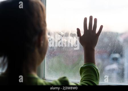 Junges Mädchen am Fenster, die Hände gegen das Fenster gedrückt, nachdenklich oder wollen heraus Stockfoto