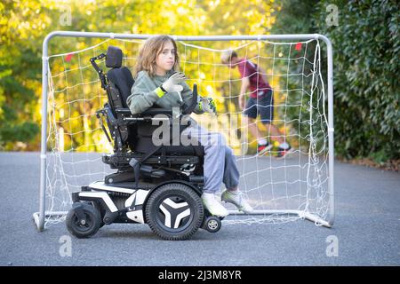 Das elfjährige Mädchen mit Ullrich kongenitaler Muskeldystrophie spielt in ihrem Rollstuhl in der Nähe ihres Heims Fußball Stockfoto