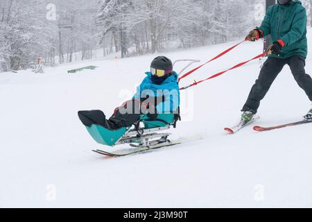 Adaptives Skifahren für ein Mädchen mit Ullrich kongenitaler Muskeldystrophie, in einem Skigebiet mit einem Instruktor Stockfoto