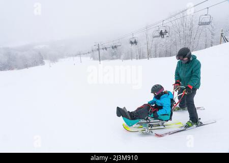 Adaptives Skifahren für ein Mädchen mit Ullrich kongenitaler Muskeldystrophie, in einem Skigebiet mit einem Instruktor Stockfoto