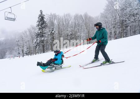 Adaptives Skifahren für ein Mädchen mit Ullrich kongenitaler Muskeldystrophie, in einem Skigebiet mit einem Instruktor Stockfoto