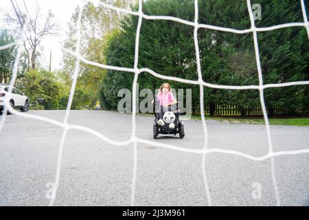 Das elfjährige Mädchen mit Ullrich kongenitaler Muskeldystrophie spielt in ihrem Rollstuhl in der Nähe ihres Heims Fußball Stockfoto