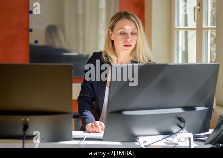 Geschäftsfrau, die in einem modernen Großraumbüro an einem Desktop-Computer sitzt und arbeitet Stockfoto