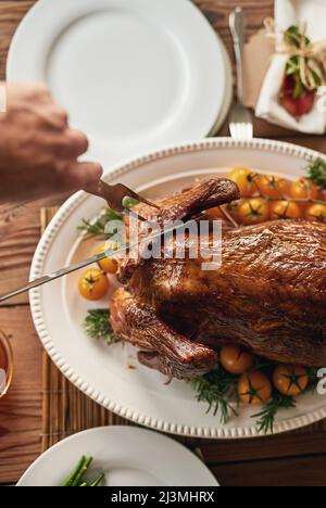 Nett und zart. Aufnahme einer nicht erkennbaren Person, die ein gebratenes Huhn für die anderen Personen zum Essen schneidet. Stockfoto