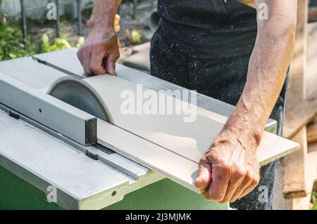 turner arbeitet an einer Drehbank. Nahaufnahme. Sägetisch. Ein Mann sägt einen Baum mit einer Fräsmaschine. Ein erfahrener Zimmermann schneidet ein Holzbrett mit einem runden s Stockfoto