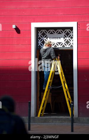 Arbeiter auf einer Leiter, die ein Ladenschild über der Tür befestigt Stockfoto
