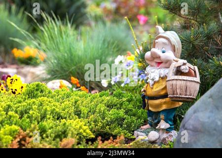 Lustiger Gartenzwerg, der zwischen schönen Blumen im Garten steht Stockfoto