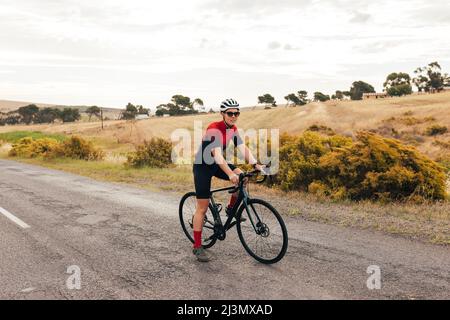 Die ganze Länge eines Profi-Radfahrers, der eine Pause von intensivem Training auf der Landstraße einnimmt Stockfoto