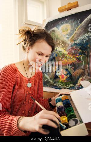 Lächelndes Mädchen malt in ihrer Werkstatt mit Ölfarben auf Leinwand. Stockfoto