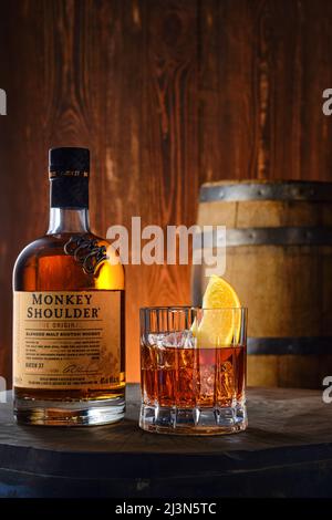 April 8,2022, Minsk, Weißrussland - Flasche und Glas mit Monkey Shoulder Blended Malt Scotch Whisky mit einem Fass auf dem Hintergrund Stockfoto