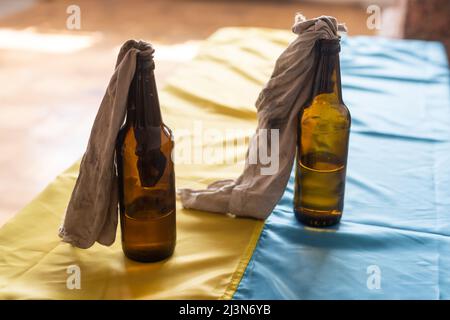 Molotow Cocktail, Kriegsrecht in der Ukraine, eine brennbare Mischung in Flaschen mit einem Lappen liegt auf der Flagge der Ukraine, Krieg Ukraine 2022 Stockfoto