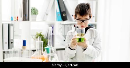 Schuljunge trägt Schutzbrille tun Chemie-Experiment Blick auf Rohr in der Grundwissenschaft Klasse. Clevere Pupille, die Flüssigkeit im Labor analysiert Stockfoto
