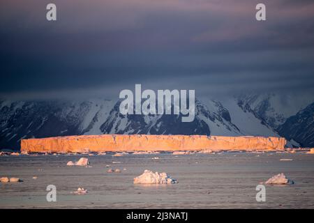 Am späten Nachmittag fällt Licht auf einen Eisberg in Tabellenform und Berge, die von einer niedrigen Wolke verdeckt werden. Marguerite Bay, Antarktis Stockfoto
