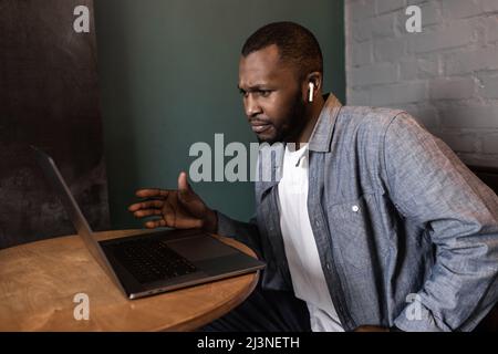 Nachdenklicher junger afroamerikanischer Geschäftsmann schaut auf Laptop-Bildschirm, denkt über einen Plan oder eine Strategie eines Online-Projekts nach, löst Probleme, Student arbeitet Stockfoto