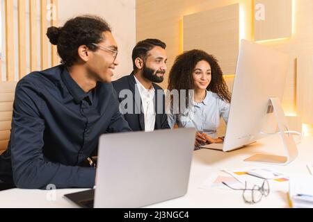 Brainstorming in einem multirassischen Team im Büro. Junger multirassischer Mann, der mit seinen Kollegen auf den Computerbildschirm schaut und sich großartig fühlt. Modernes Büro Stockfoto