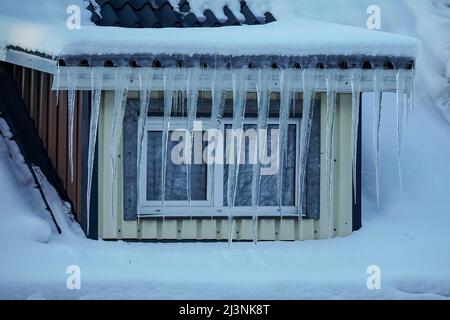 Lange durchsichtige Eiszapfen, die vom Dach vor dem Fenster des Hauses hängen Stockfoto