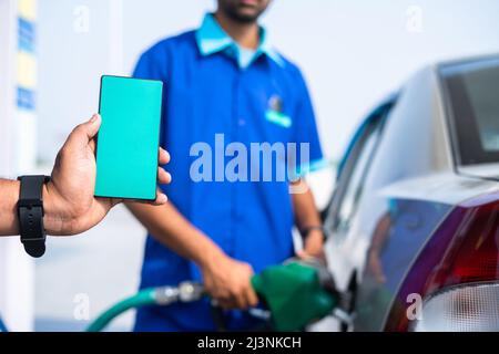 Nahaufnahme der Hand zeigt grünes Handy, während Arbeiter Benzin auf das Auto füllen - Konzept der Anwendung Werbung, Werbung und Stockfoto