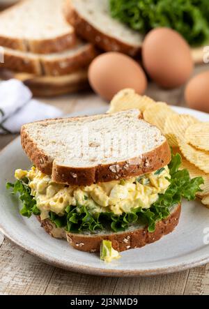 Eiersalat und Salat-Sandwich auf Vollkornbrot mit Kartoffelchips auf einem Teller Stockfoto