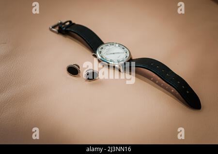Manschettenknöpfe für Männer und eine Uhr mit schwarzem Armband auf einem Hintergrund Stockfoto