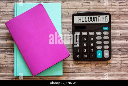 Das Konzept der Finanzbuchhaltung wurde auf einem Rechner geschrieben. Bunte Notizbücher auf einem Holzhintergrund Stockfoto