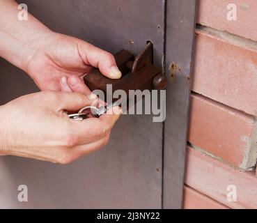 Die Hände der Frauen öffnen ein rostetes Schloss mit Schlüsseln. An einer Metalltür verriegeln. Sicherheit. Stockfoto