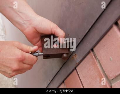 Die Hände der Frauen öffnen ein rostetes Schloss mit Schlüsseln. An einer Metalltür verriegeln. Sicherheit. Stockfoto