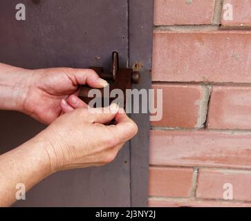 Die Hände der Frauen öffnen ein rostetes Schloss mit Schlüsseln. An einer Metalltür verriegeln. Sicherheit. Stockfoto