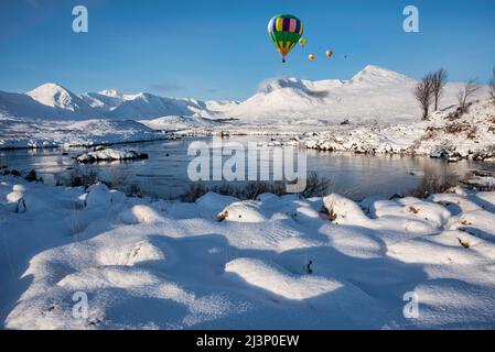 Digitales Composite-Bild von Heißluftballons, die über die majestätische Winterlandschaft fliegen, mit Blick auf die Berge der schottischen Highlands über Loch Stockfoto