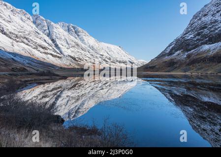 Wunderschöne Winterlandschaft von Loch Achtriochan in den schottischen Highlands mit atemberaubenden Reflexionen in stillem Wasser mit tiefblauem Himmel Stockfoto