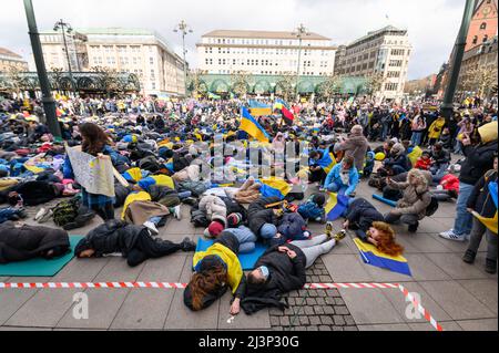 Hamburg, Deutschland. 09. April 2022. Demonstranten lügen und stehen während einer Protestaktion am Rathausmarkt. Mehrere hundert Menschen protestierten am Samstag in einer kraftvollen Aktion am Hamburger Rathausmarkt gegen den Krieg in der Ukraine. Einige der Demonstranten stellten die grausamen Bilder von Zivilisten nach, die in den Kiewer Vororten Butscha, Irpin und Hostomel getötet wurden: Wie Kriegsopfer, einige blutüberströmt und mit gefesselten Händen, legten sie sich auf den Platz vor dem Rathaus. Das Wehklagen der Sirenen war zu hören. Quelle: Jonas Walzberg/dpa/Alamy Live News Stockfoto