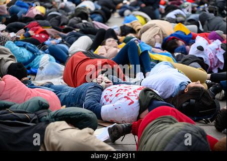 Hamburg, Deutschland. 09. April 2022. Demonstranten lügen und stehen während einer Protestaktion am Rathausmarkt. Mehrere hundert Menschen protestierten am Samstag in einer kraftvollen Aktion am Hamburger Rathausmarkt gegen den Krieg in der Ukraine. Einige der Demonstranten stellten die grausamen Bilder von Zivilisten nach, die in den Kiewer Vororten Butscha, Irpin und Hostomel getötet wurden: Wie Kriegsopfer, einige blutüberströmt und mit gefesselten Händen, legten sie sich auf den Platz vor dem Rathaus. Das Wehklagen der Sirenen war zu hören. Quelle: Jonas Walzberg/dpa/Alamy Live News Stockfoto