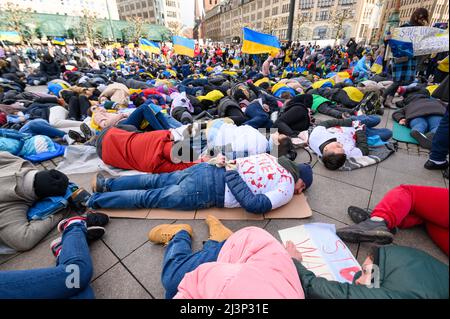 Hamburg, Deutschland. 09. April 2022. Demonstranten lügen und stehen während einer Protestaktion am Rathausmarkt. Mehrere hundert Menschen protestierten am Samstag in einer kraftvollen Aktion am Hamburger Rathausmarkt gegen den Krieg in der Ukraine. Einige der Demonstranten stellten die grausamen Bilder von Zivilisten nach, die in den Kiewer Vororten Butscha, Irpin und Hostomel getötet wurden: Wie Kriegsopfer, einige blutüberströmt und mit gefesselten Händen, legten sie sich auf den Platz vor dem Rathaus. Das Wehklagen der Sirenen war zu hören. Quelle: Jonas Walzberg/dpa/Alamy Live News Stockfoto