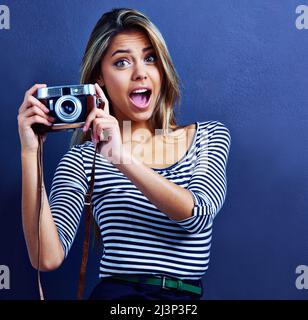 Halte die Pose. Aufnahme einer überraschten jungen Frau mit einer Kamera. Stockfoto