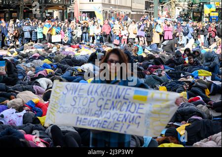 Hamburg, Deutschland. 09. April 2022. Demonstranten lügen und stehen während der Protestaktion am Rathausmarkt. Mehrere hundert Menschen protestierten am Samstag auf dem Hamburger Rathausmarkt mit einer einschneidigen Aktion gegen den Krieg in der Ukraine. Einige der Demonstranten stellten die grausamen Bilder von Zivilisten nach, die in den Kiewer Vororten Butscha, Irpin und Hostomel getötet wurden: Wie Kriegsopfer, einige blutüberströmt und mit gefesselten Händen, legten sie sich auf den Platz vor dem Rathaus. Das Wehklagen der Sirenen war zu hören. Quelle: Jonas Walzberg/dpa/Alamy Live News Stockfoto