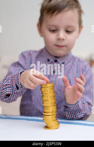 Turm der Münzen. Ein kleiner Junge baut eine Säule aus Goldmünzen. Stockfoto