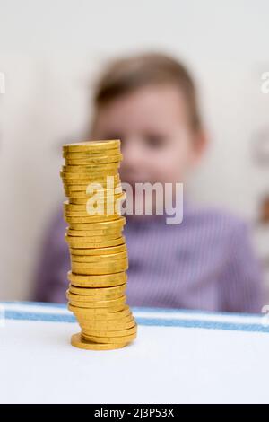 Turm der Münzen. Ein kleiner Junge baut eine Säule aus Goldmünzen. Stockfoto