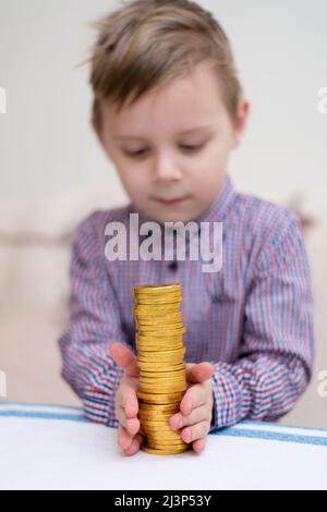 Turm der Münzen. Ein kleiner Junge baut eine Säule aus Goldmünzen. Stockfoto