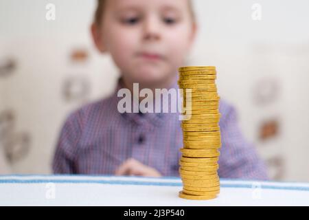 Turm der Münzen. Ein kleiner Junge baut eine Säule aus Goldmünzen. Stockfoto