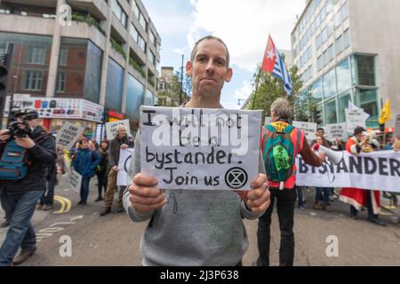 London, Großbritannien. April 2022. Etienne Stott MBE, Olympiasiegerin im Kanu aus London 2012, hält ein Schild mit der Aufschrift „Ich werde kein Zuschauer sein. Begleiten Sie uns“ mit dem Symbol der Extinction Rebellion während eines Straßenprotests im Zentrum Londons. Die Demonstration zeigt Banner, Fahnen und Teilnehmer, die sich für Klimaschutz und Umweltgerechtigkeit einsetzen. Fotografen und Aktivisten kommen in einer friedlichen Versammlung zusammen, um das Engagement der Bürger und die Mobilisierung der Basis hervorzuheben. Penelope Barritt/Alamy Live News Stockfoto