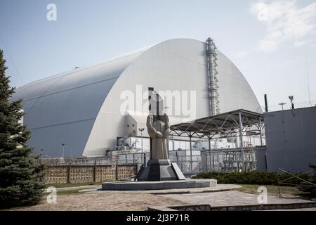 Tschernobyl, Ukraine. 10. April 2019. Die Katastrophe von Tschernobyl, Momument zu Liquidatoren dedizierte sitzt in der Nähe der neuen Schutzkonstruktion, welche die Reste der Reaktor Nummer 4 im Kernkraftwerk Tschernobyl, in der Katastrophe von Tschernobyl im Jahr 1986 zerstört. Die Anlage befindet sich jetzt in der Sperrzone von Tschernobyl in der Ukraine. Stockfoto