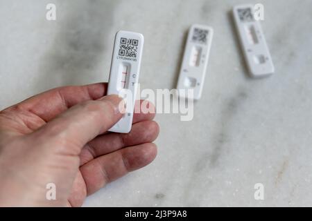 Selbst- oder selbst verabreichte laterale Schnellflusstests (Rapid lateral flow Tests, LFT) für COVID-19 Coronavirus, positiv und negativ; Hand mit positivem Ergebnis Stockfoto