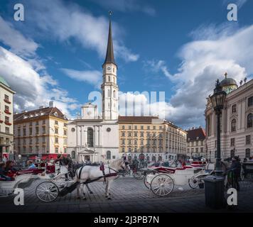 St. Michael Platz (Michaelerplatz) mit St. Michael Kirche und Pferdekutschen (Fiaker) - Wien, Österreich Stockfoto