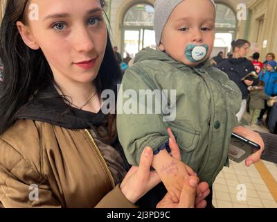 Przemysl, Polen. 8. April 2022. Eine ukrainische Mutter am Bahnhof Przemysl in Polen, eine neu angereiste Flüchtling, schreibt den Namen ihres Babys auf seine Hand, falls er sich verlaufen sollte. (Bild: © Amy Katz/ZUMA Press Wire) Stockfoto