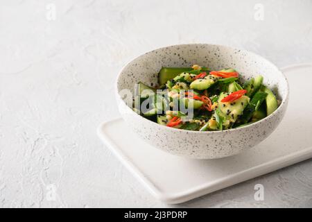 Asiatisch würzige Salatgurken mit frischem Koriander, Ingwer, Chilischote, schwarzem Essig auf weißem Tisch. Beliebte chinesische kalte Vorspeise. Nahaufnahme. Stockfoto