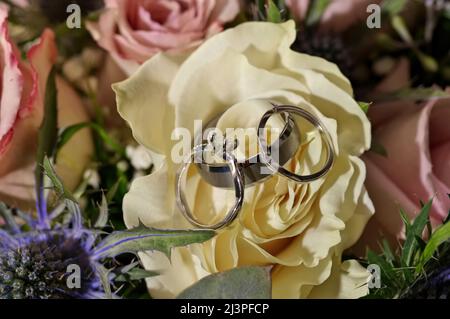 Hochzeit und Verlobungsringe in Weißgold und Diamanten auf weißem und rosafarbenem Rosenstrauß Stockfoto