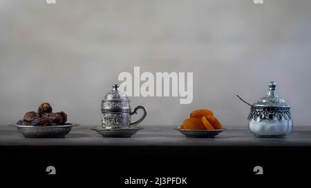 Silberne Kaffeetasse und Zuckergläser mit Datteln und getrockneten Aprikosen, heller Hintergrund Stockfoto