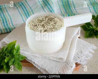 Rundkäse in einer Käseform mit getrockneten Kräutern und frischem Basilikum, selektiver Fokus. Hausgemachtes Milchprodukt Stockfoto