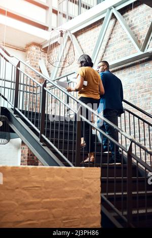 Die Treppe zum Erfolg führen. Aufnahme von zwei Designern, die eine Diskussion über eine Treppe in einem Büro führen. Stockfoto