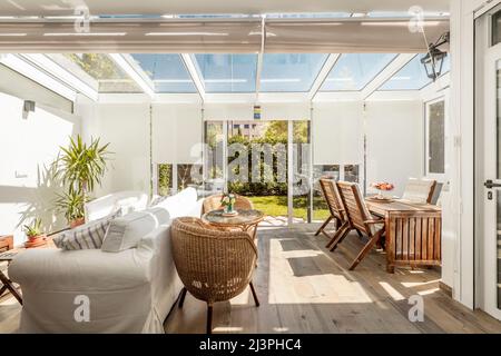 Terrasse mit Zugang zum Garten mit weißer Aluminiumschreinerei und Glas mit großen Schiebetüren mit hellen Holzböden und Korbmöbeln und einem Stockfoto